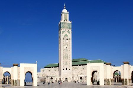 Vista panorámica de la mezquita Hassan II de Casablanca con su minarete central y arcos monumentales en la explanada bajo el cielo azul