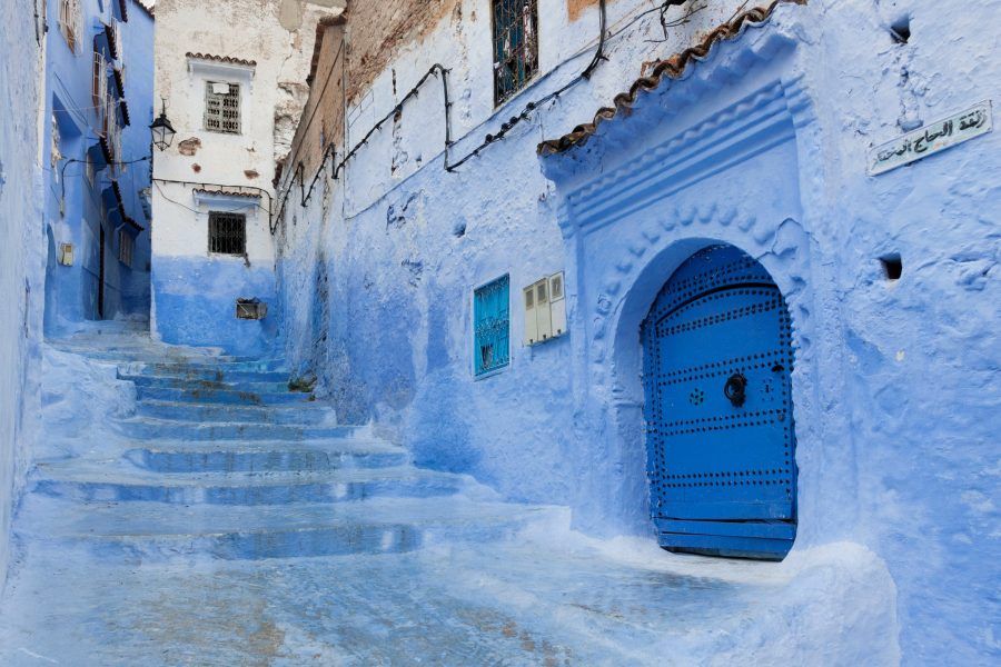 Escaleras azules y puerta tradicional de herrajes en una callejuela de la medina de Chefchaouen
