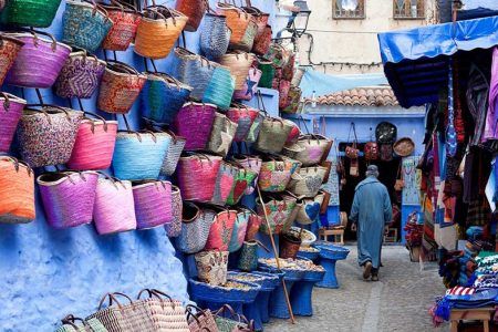 Cestas de palma coloridas colgadas en la pared azul de Chefchaouen junto a tiendas de artesanía