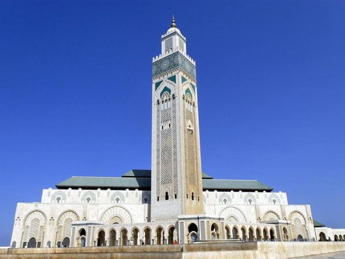 Vista exterior de la mezquita Hassan II de Casablanca con su minarete decorado bajo un cielo azul y la fachada de mármol blanco