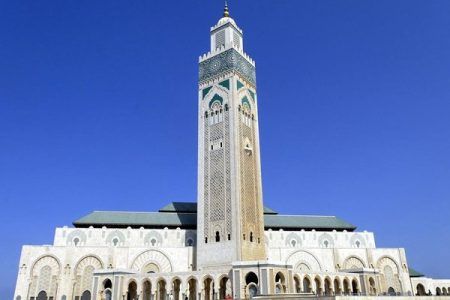 Vista exterior de la mezquita Hassan II de Casablanca con su minarete decorado bajo un cielo azul y la fachada de mármol blanco