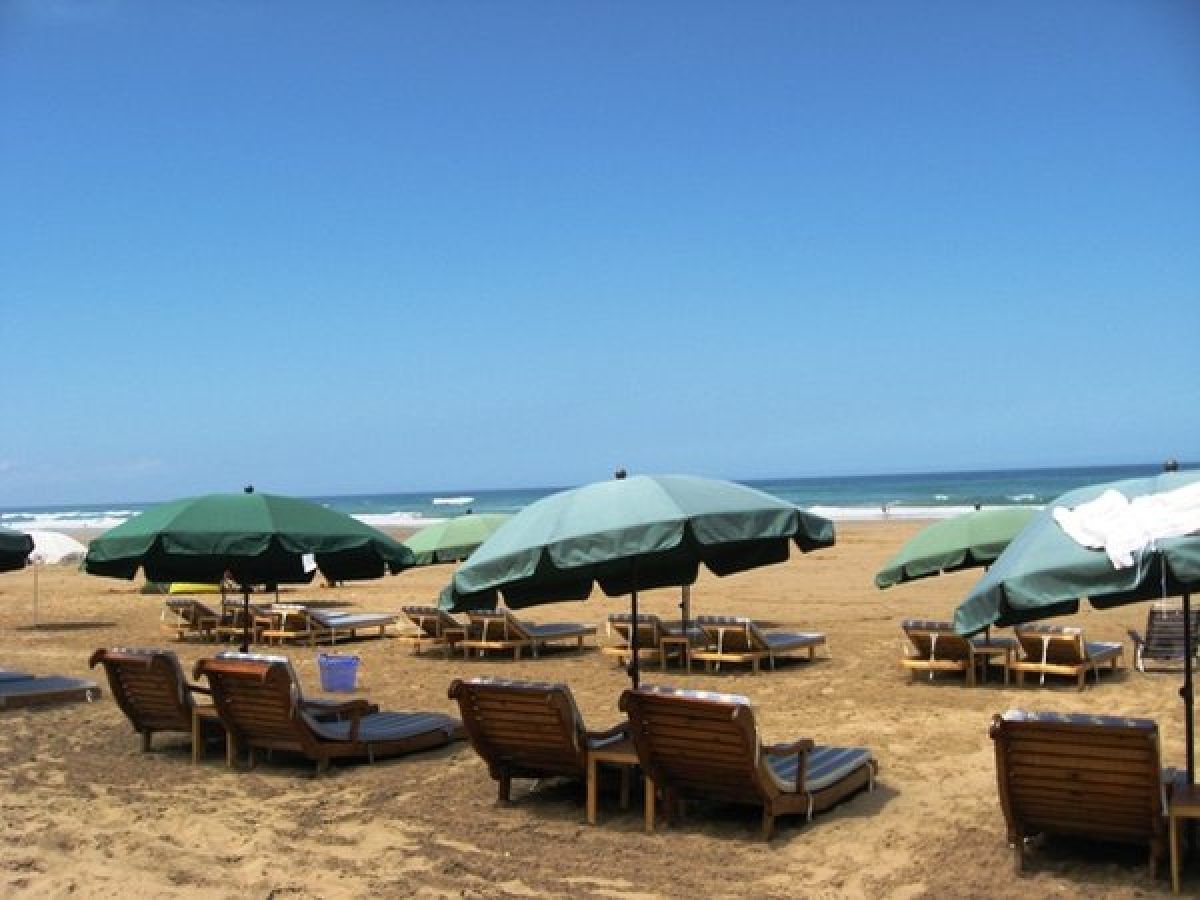 Playa de Asilah con tumbonas de madera y sombrillas verdes frente al océano Atlántico en el norte de Marruecos