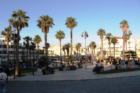 Plaza de Tánger con palmeras, viajeros y locales sentados disfrutando al atardecer