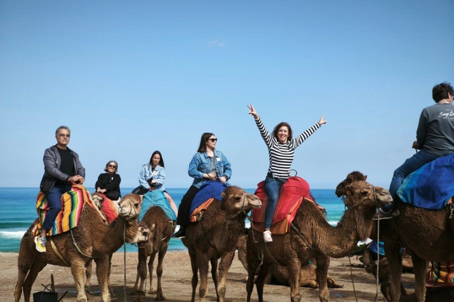 Viajeras montando camellos en la playa del norte de Marruecos con el Atlántico al fondo