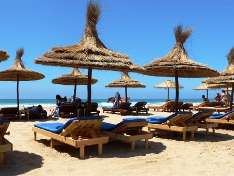 Hamacas de madera y sombrillas de paja en la playa de Asilah en verano con el océano Atlántico y cielo azul despejado