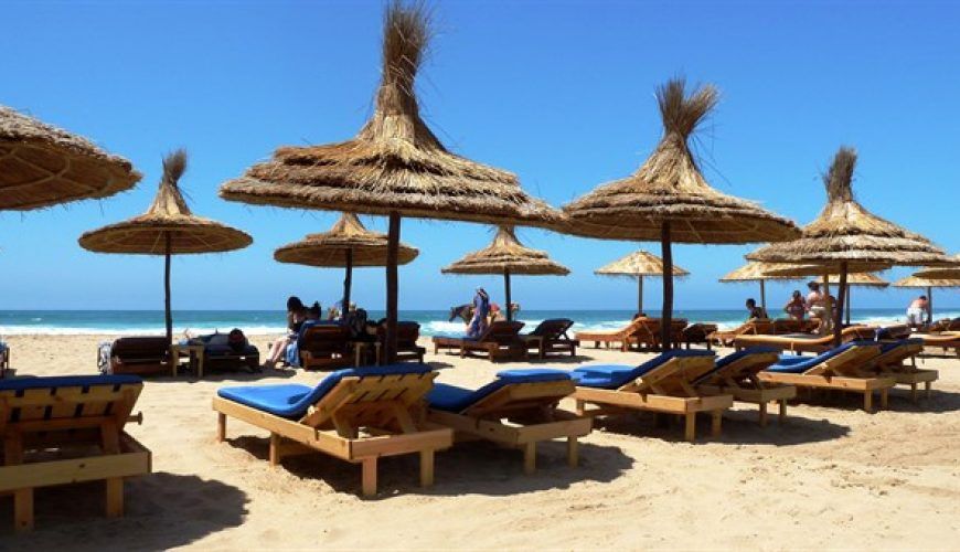 Hamacas de madera y sombrillas de paja en la playa de Asilah en verano con el océano Atlántico y cielo azul despejado