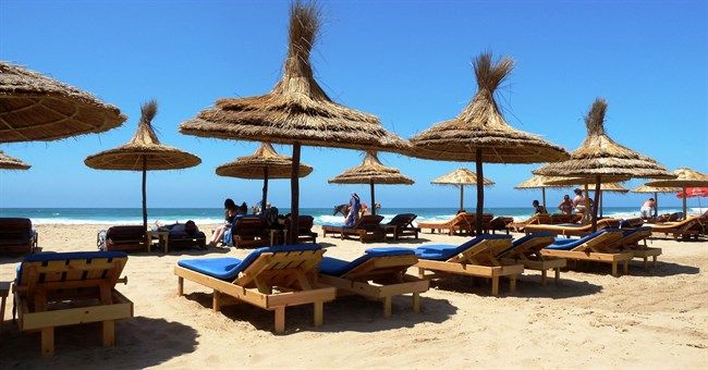 Hamacas de madera y sombrillas de paja en la playa de Asilah en verano con el océano Atlántico y cielo azul despejado