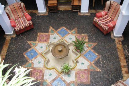 Patio central de la Casa Hassan en Chefchaouen visto desde arriba, con fuente de mosaico y mobiliario tradicional marroquí