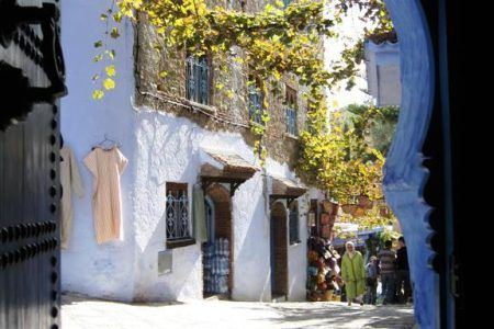 Vista a través de un arco morisco de la entrada de la Casa Hassan hacia una calle soleada de la medina de Chefchaouen