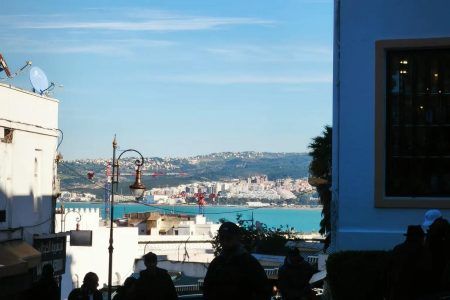 Vista de la bahía y el puerto de Tánger desde la medina al atardecer con siluetas de viajeros en primer plano