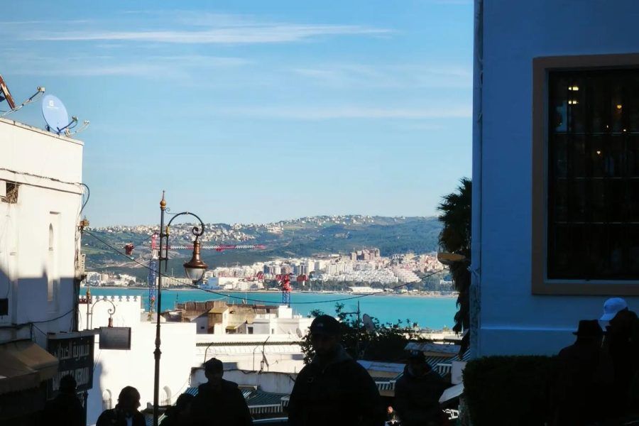 Vista de la bahía y el puerto de Tánger desde la medina al atardecer con siluetas de viajeros en primer plano