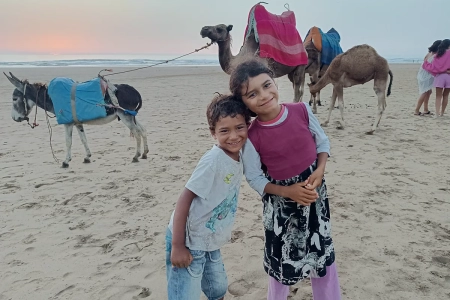 Niños locales con camellos y burro en la playa de Asilah al atardecer