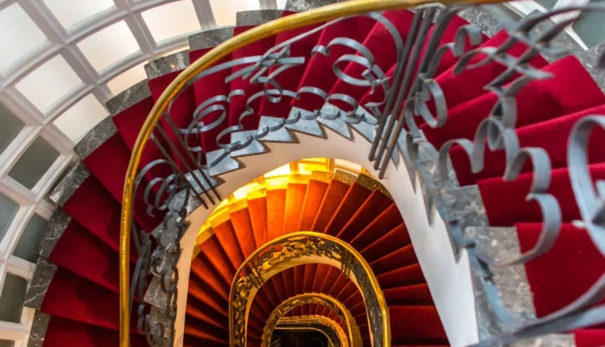 Escalera de caracol con barandilla dorada y alfombra roja en el Hotel Le Doge de Casablanca