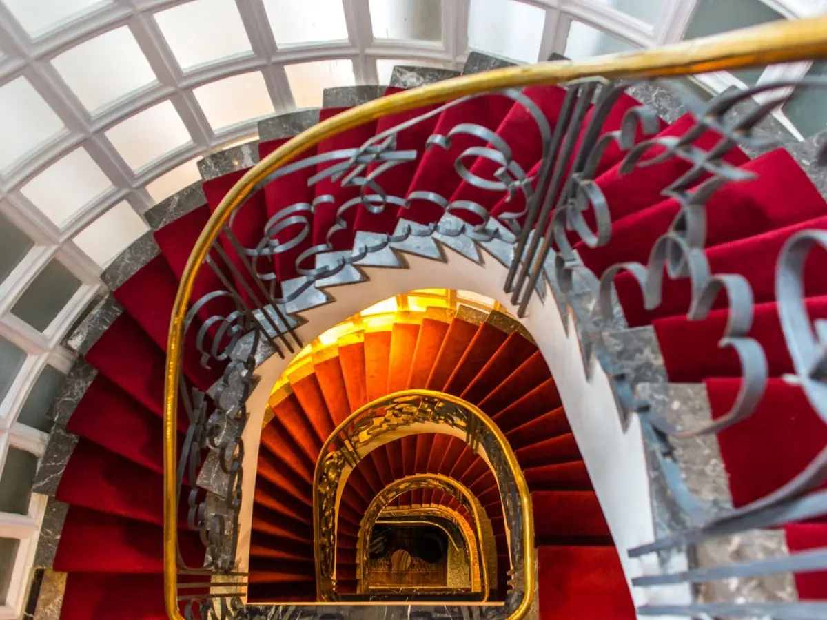 Escalera de caracol con barandilla dorada y alfombra roja en el Hotel Le Doge de Casablanca