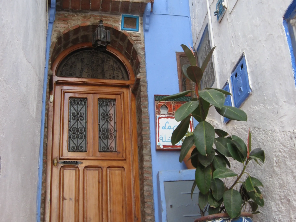 Puerta de entrada de madera tallada con maceta azul y planta en Casa La Palma, Chefchaouen