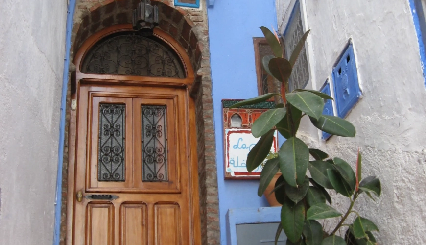 Puerta de entrada de madera tallada con maceta azul y planta en Casa La Palma, Chefchaouen