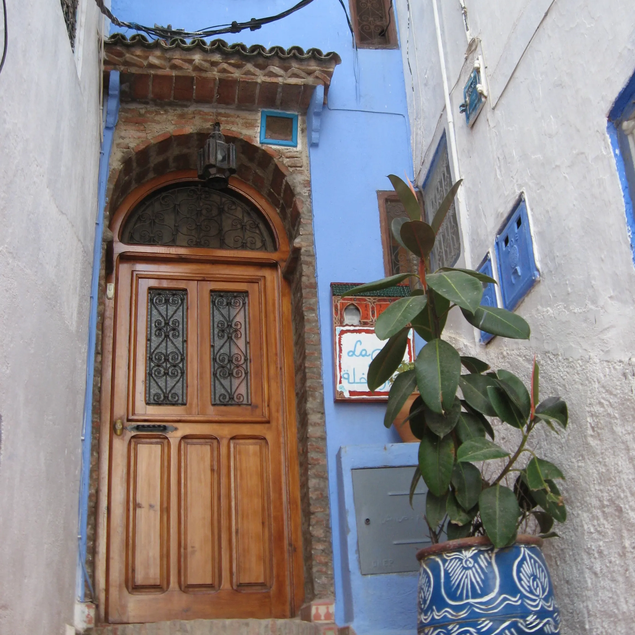 Puerta de entrada de madera tallada con maceta azul y planta en Casa La Palma, Chefchaouen