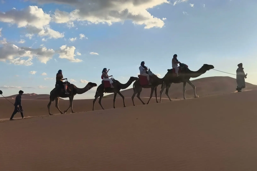 Caravana de camellos cruzando las dunas de Merzouga bajo el cielo al atardecer